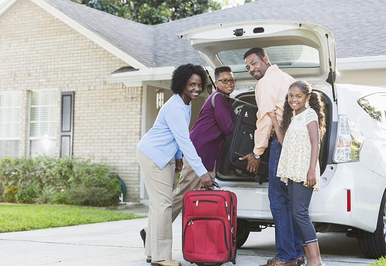 A family with mother, son, father, and daughter packing luggage in the trunk of their car.