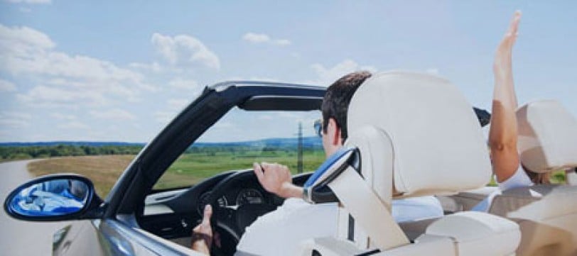 Two people driving down a road in a convertible with the top down